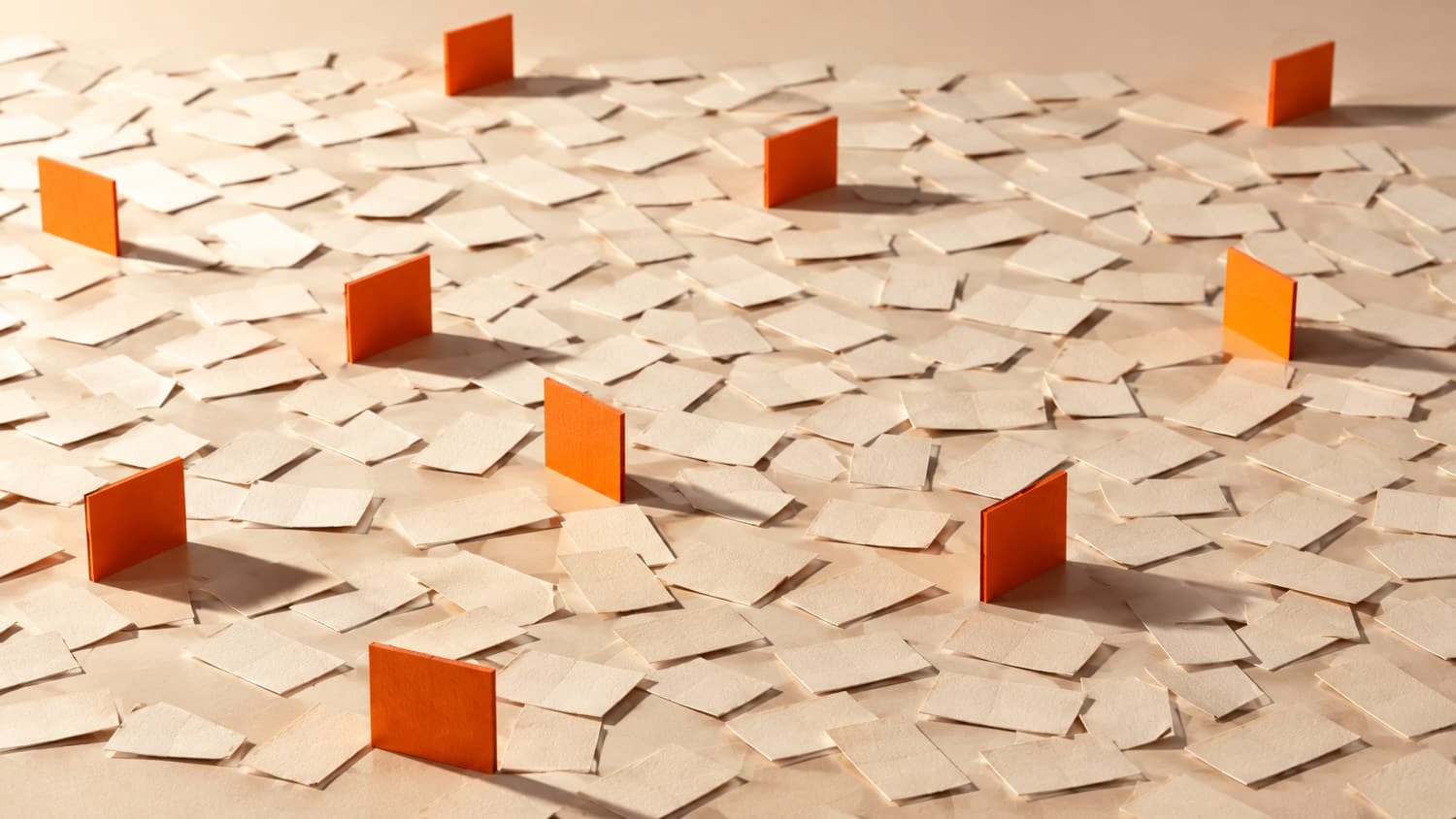 A wide field of bone-white paper slips lying flat with a scattered handful of bright orange slips standing upright among them